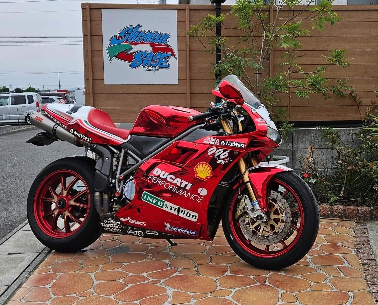 参考写真：青空の下、店先に停まる赤いバイクと看板